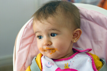 Primer plano de un bebé con ojos azules con la cara llena de potito mirando hacia un lado
