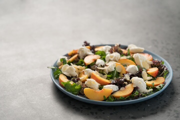 salad with nectarines, mozzarella and mixed greens in blue plate on concrete background with copy space