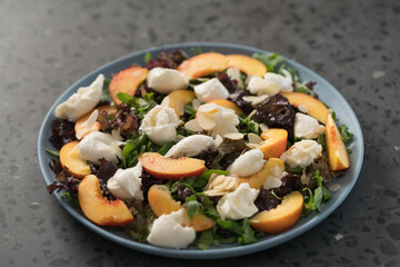 salad with nectarines, mozzarella and mixed greens in blue plate on concrete background