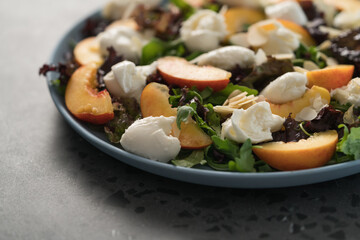 salad with nectarines, mozzarella and mixed greens in blue plate on concrete background