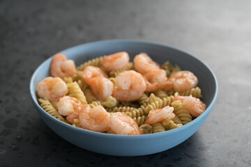 Fusilli with shrimps and pesto in a blue bowl on concrete background