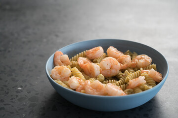 Fusilli with shrimps and pesto in a blue bowl on concrete background