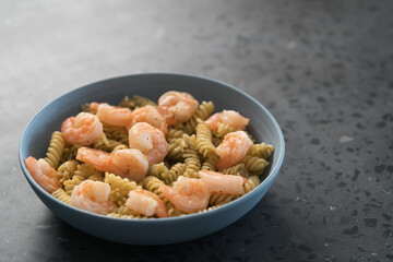 Fusilli with shrimps and pesto in a blue bowl on concrete background