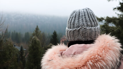 Rear view of a woman mountain tourist in a pink jacket with fur and a gray knitted hat against a...