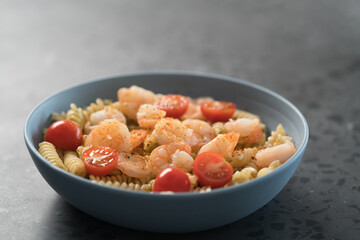 Fusilli with shrimps, cherry tomatoes and pesto in a blue bowl on concrete background