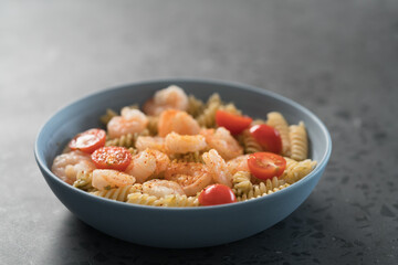 Fusilli with shrimps, cherry tomatoes and pesto in a blue bowl on concrete background