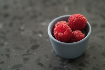 Fresh ripe raspberries in small blue bowl on concrete background