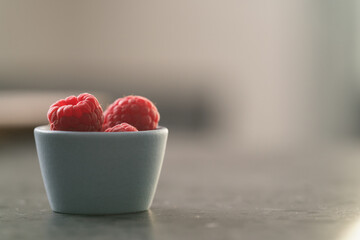 Fresh ripe raspberries in small blue bowl on concrete countertop