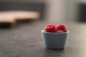 Fresh ripe raspberries in small blue bowl on concrete countertop