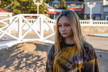 Fototapeta premium A beautiful young girl, blonde, in fashionable clothes stands on a sandy beach and looks thoughtfully into the distance. Resort city of Gelendzhik