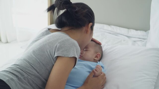  young Asian mother tenderly kisses her daughter's forehead.
