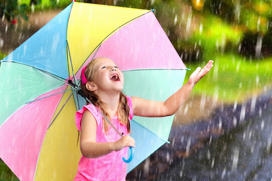 Kid with umbrella playing in summer rain.