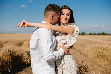 Young couple in the wheat field on sunny summer day. Couple in love have fun in golden field. Romantic couple in casual clothe outdoodrs on boundless field