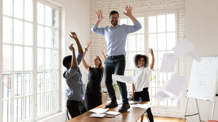 Overjoyed diverse multiracial colleagues have fun at meeting throw papers laugh entertain together,...