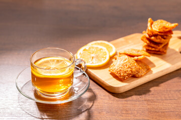 Glass of hot tea with lemon and Thai rice cracker on wood table.