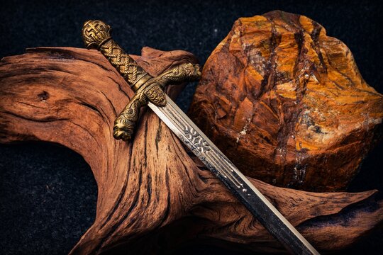 Knight's sword on the background of an old textured wooden driftwood and a rough stone of brown color