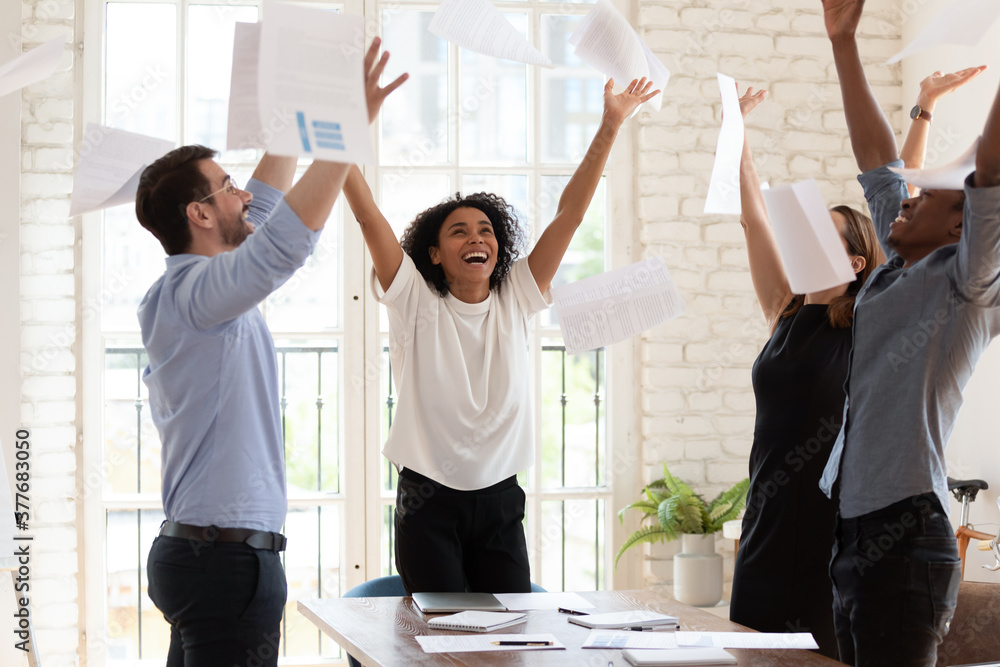 Wall mural Overjoyed young multiracial businesspeople throw paper up in air feel excited about successful startup project, happy multiethnic colleagues have fun celebrate business success at office meeting