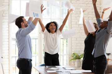 Overjoyed young multiracial businesspeople throw paper up in air feel excited about successful...