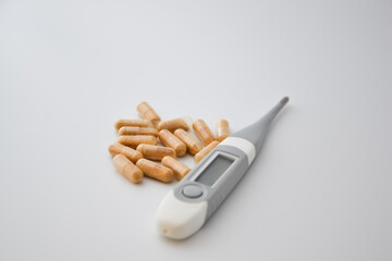 Group of natural pills on a white background with a grey thermometer