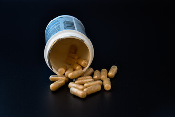 Medication bottle and natural pills spilled on black background. Medication and prescription pills flat lay background