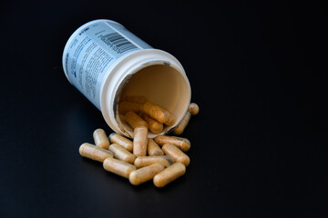 Medication bottle and natural pills spilled on black background. Medication and prescription pills flat lay background
