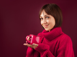 young beautiful woman in a red sweater with a Cup of tea in her hands on a plain background, space for text