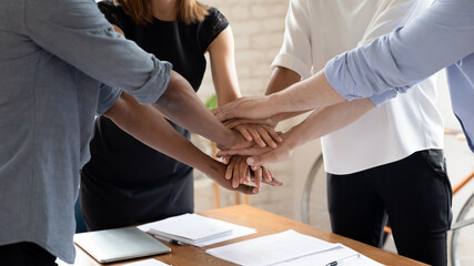 Close up of diverse multiethnic colleagues stack hands in pile show support and help, motivated multicultural coworkers engaged in teambuilding activity at office meeting, teamwork concept