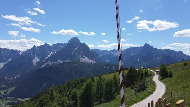 4k video shooting with drone of mountain panoramas, on the italian dolomites alps. snow-capped peaks, green meadows and ski slopes, mountain trails with small wooden houses. blue skies with clouds.