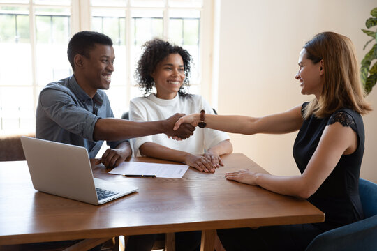 Excited African American couple shake hands get acquainted greeting with smiling female Caucasian real estate agent at office meeting, biracial husband handshake realtor close deal make agreement