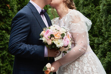Happy bride and groom walking in garden and kiss on wedding day at summer. Wedding couple in love, newlyweds, copy space