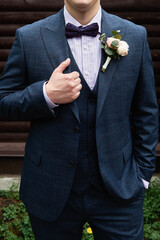 Happy groom in lilac shirt, blu suit and bow tie with buttonhole standing on wood brown background outdoors, copy space. Wedding concept