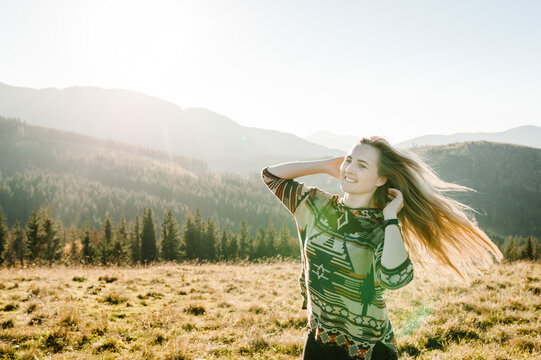Portrait of a beautiful woman smiling and looking away at mountains during sunset. Happy cheerful hipster. Girl laughing in the autumn field. World Tourism Day. Closeup.