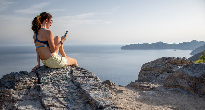 A woman taking pictures with her phone of the sea view over a mountain