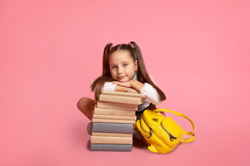 New knowledge for little schoolgirl. Child with backpack sits near stack of books