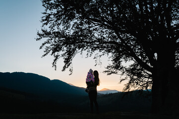 Silhouette of mom hugging daughter and looking at mountains during sunset. Autumn evening. Back view.