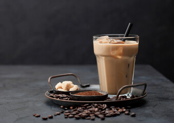 Glass of iced coffee drink with straw on tray with coffee beans and ground coffee with cane sugar...
