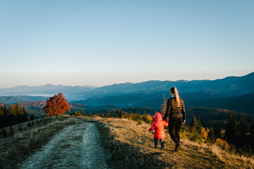 Mom and daughter, enjoying time together, walking on sunset on top of foggy mountain. Tourists on background autumn nature. Hikers on sunlight in trip in country Europe. Back view. Happy family.