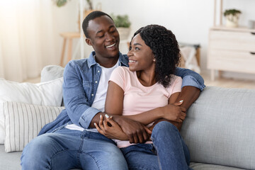 Happy african couple cuddling on sofa at home