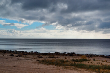 sandy shore with grass on coast of blue Ladoga northern lake at sunset with clouds in the sky