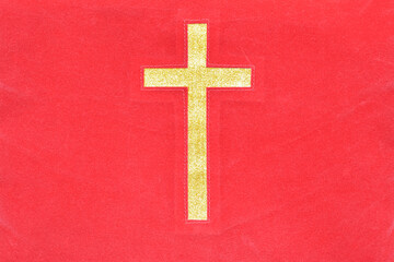 Gold catholic cross on red cloth texture background.