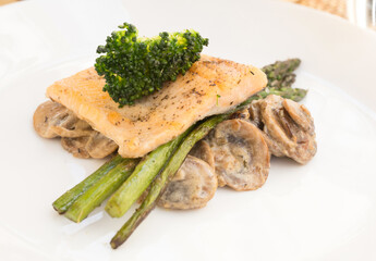 dish of fried river trout fillet with garnish of broccoli, asparagus sprouts and mushroom sauce on white background