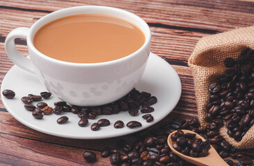 Hot coffee in a white mug on a table with coffee beans in a bag and a wooden spoon.