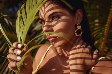 Portrait of a beautiful brunette woman in bikini with palm leaf shadows on her face. Summer happy vacation on the sea beach