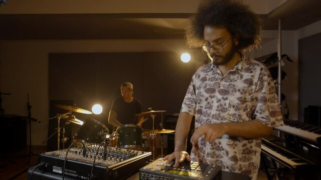Music production studio. Beatmaking. Hispanic man recording new beats and caucasian man playing drums. Talented and creative persons record their ideas.