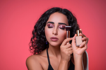 Pretty lady with bright make up with bottle of liquid foundation and brush in her hands....