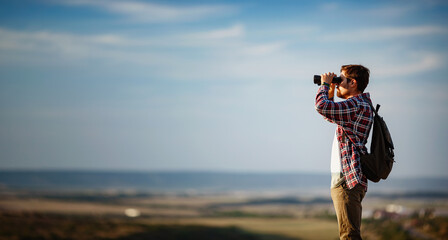 Guy looking at binoculars in hill. man in t-shirt with backpack.
