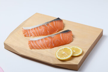 Raw salmon fillet on wooden cutting board, white background
