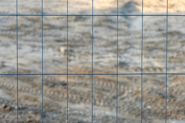 Nahaufnahme: Details eines Bauzaun zur Sicherung einer Baustelle, Baugrundstück verschwommen im Hintergrund - selektiver Fokus mit sehr wenig Tiefenschärfe