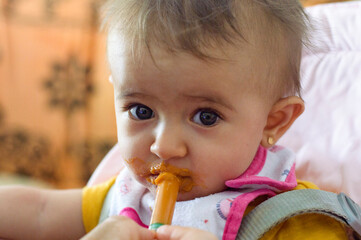 Primer plano de un bebé con ojos claros comiendo con jeringa mirando a la cámara