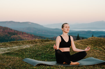 Fototapeta na wymiar A young woman is practicing yoga at mountains. Relaxing in nature. Young girl doing yoga fitness exercise outdoor in the beautiful landscape. Morning sunrise, Namaste Lotus pose. Meditation.